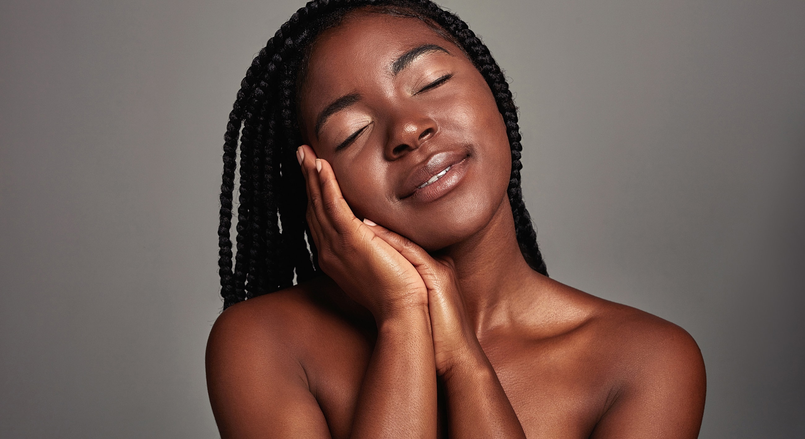 Smiling woman with braided hair, eyes closed.